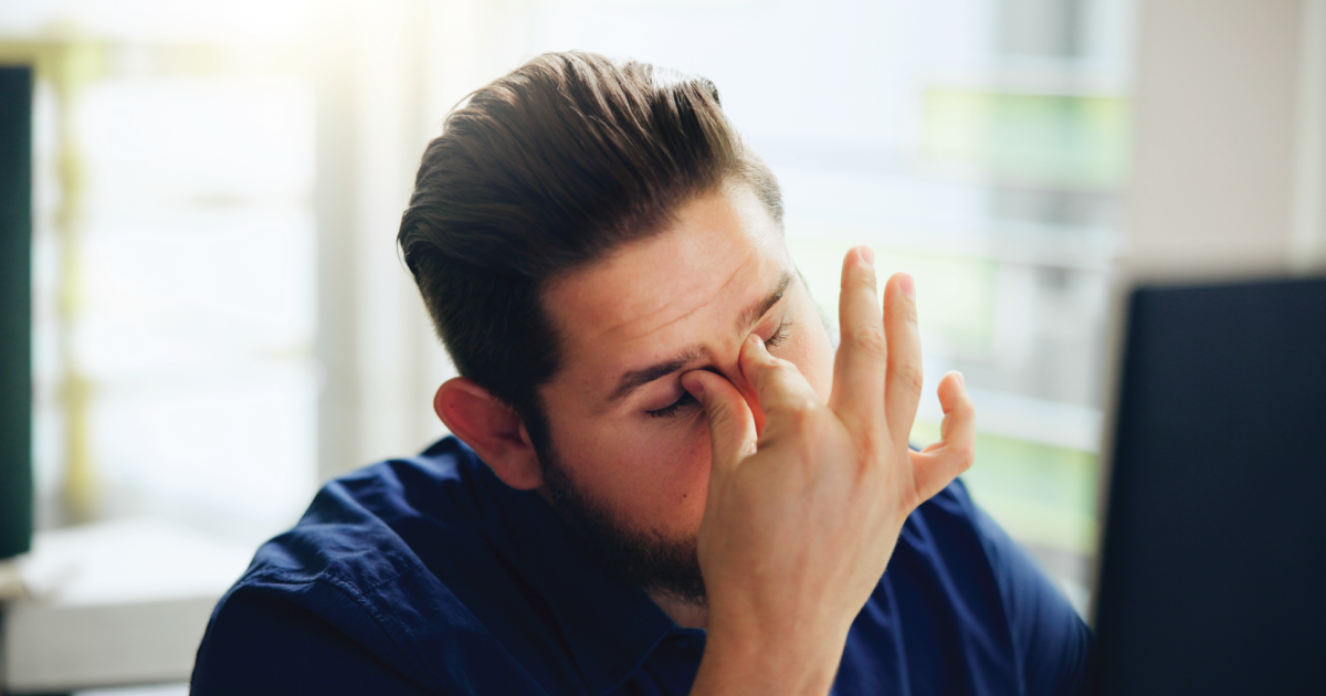 Person in a navy shirt pinching the bridge of their nose, looking in pain.