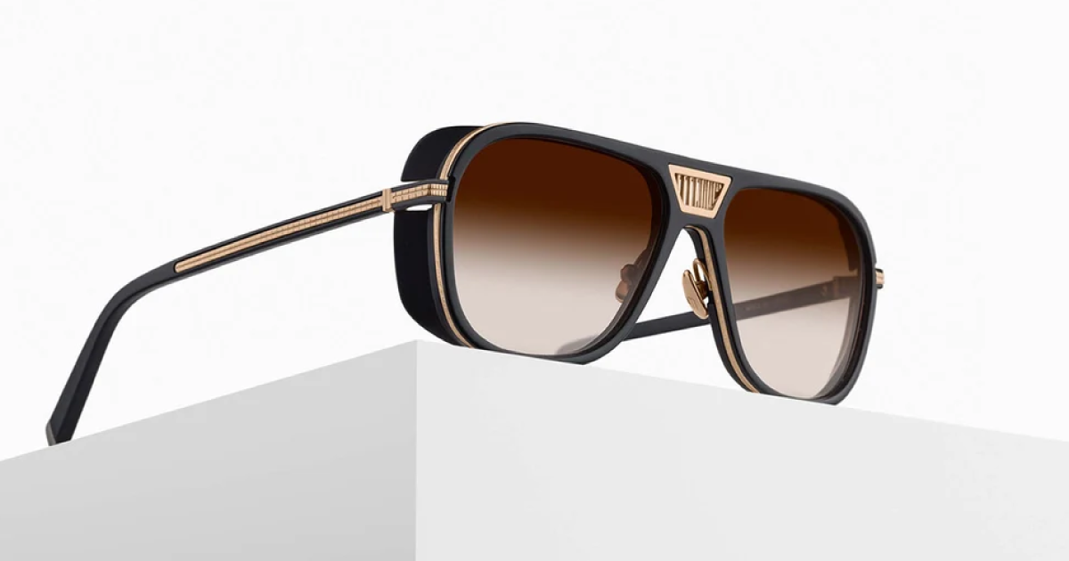 Brown-tinted sunglasses with gold accents, resting on a white geometric surface.