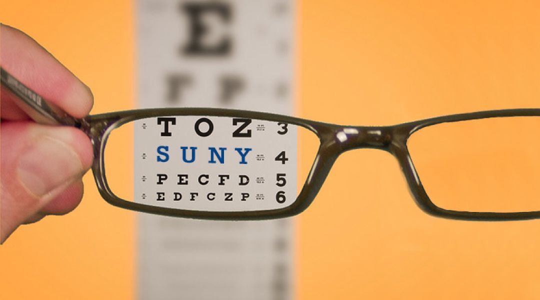 A pair of glasses held in front of an eye chart with only the view through the lens being clear