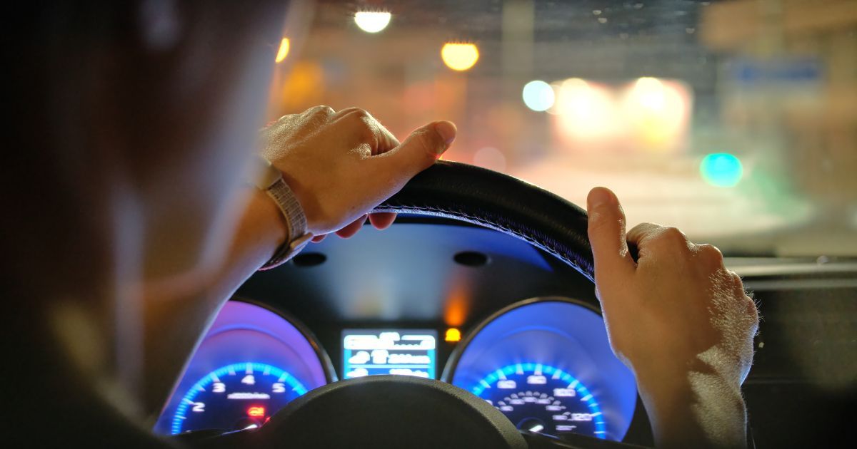 A person is driving a car at night with their hands on the steering wheel