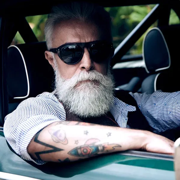 Hipster man with beard wearing black sunglasses sitting in a car