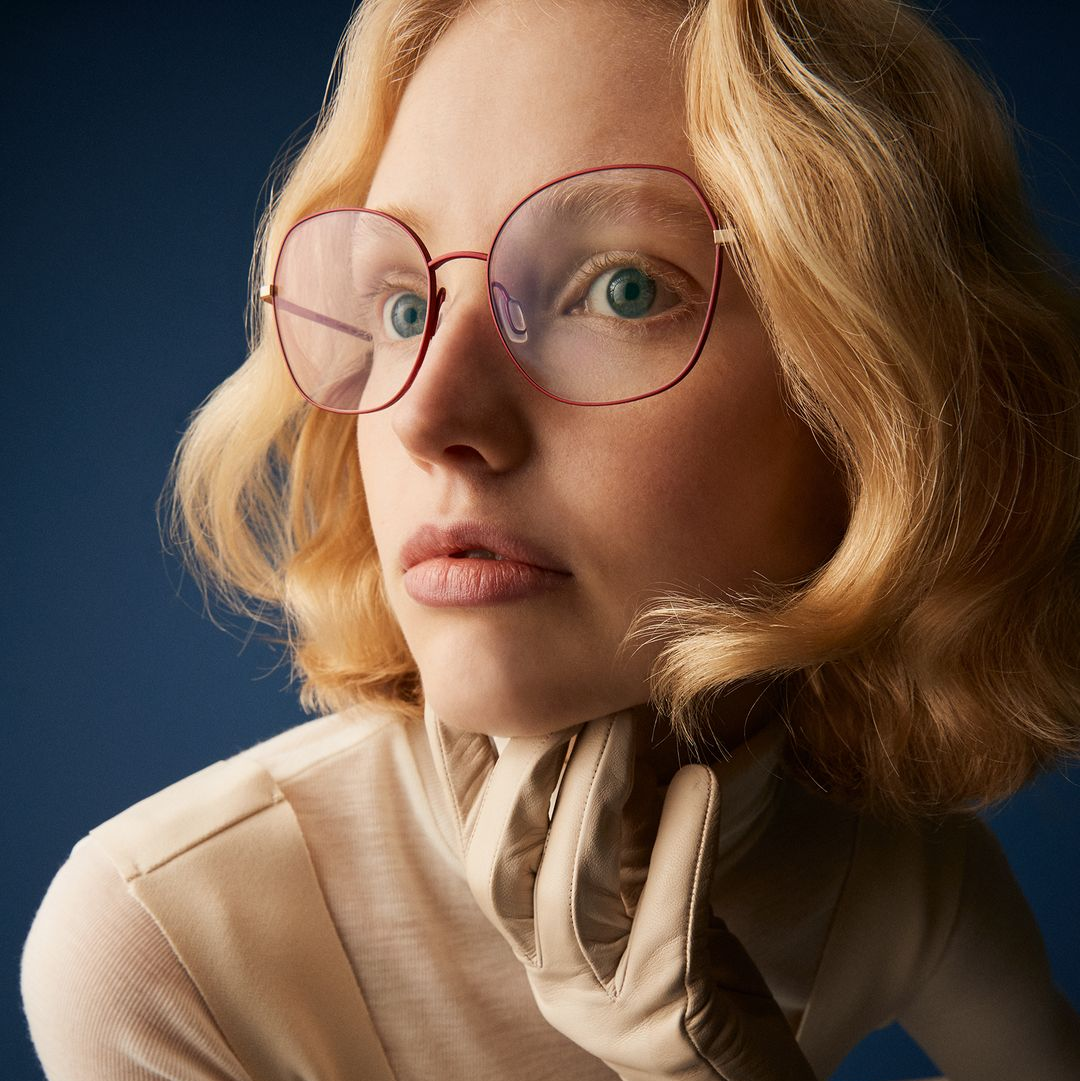Woman with her hand to her chin wearing a red Orgreen frame
