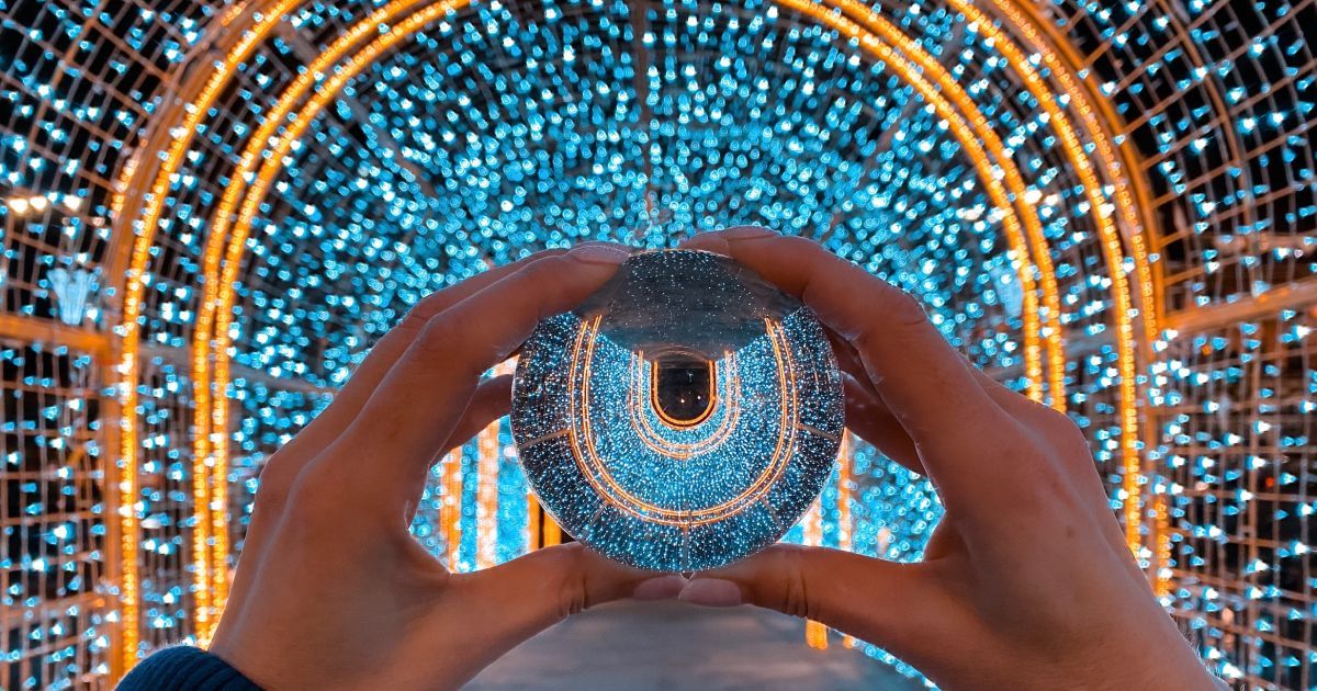 A person is holding a glass ball in front of a tunnel of lights.