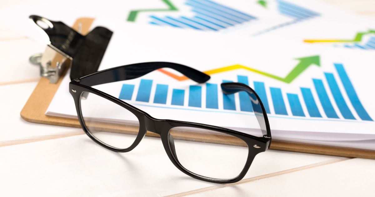 A pair of glasses is sitting on top of a clipboard with a graph showing rising profits on it.
