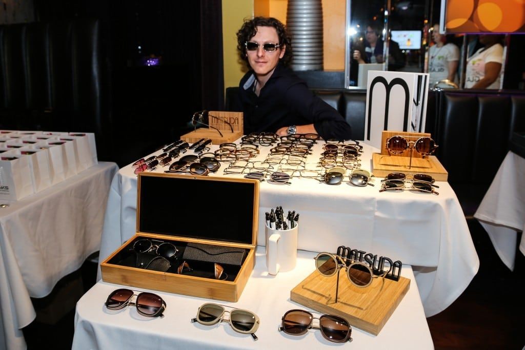 Person in sunglasses sitting at vendor table at 2015 Raise Your Glasses event