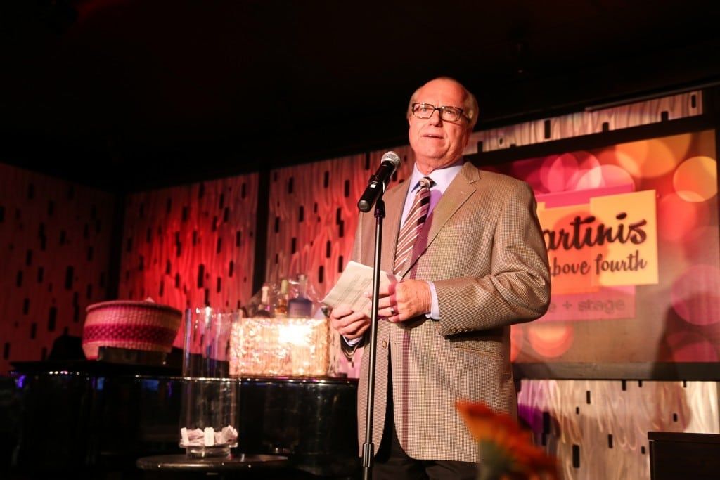 Man speaking at microphone at 2015 Raise Your Glasses event at Martinis Above Fourth
