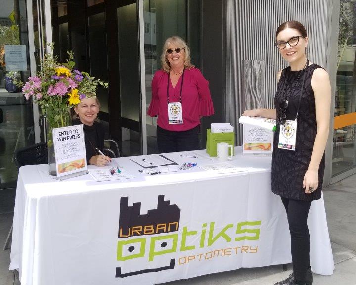 3 staff people at reception table covered in Urban Optiks Optometry logo tablecloth