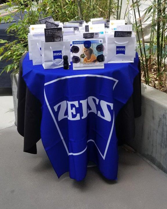 Blue tablecloth with Zeiss logo and small shopping bags on table at 2019 Raise Your Glasses Event