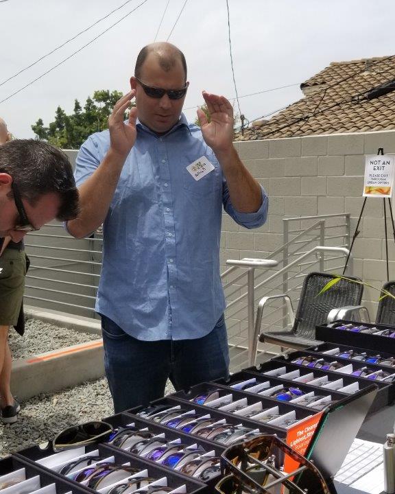 Person in blue shirt trying on sunglasses at Raise Your Glasses 2019 Event