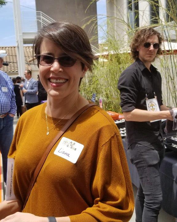 Smiling person in burnt orange blouse and man in background