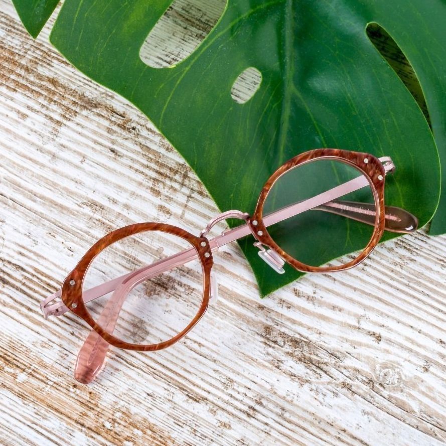 A pair of round tortoise and pink Say-oh glasses sitting on top of a large banana leaf on a wooden table.