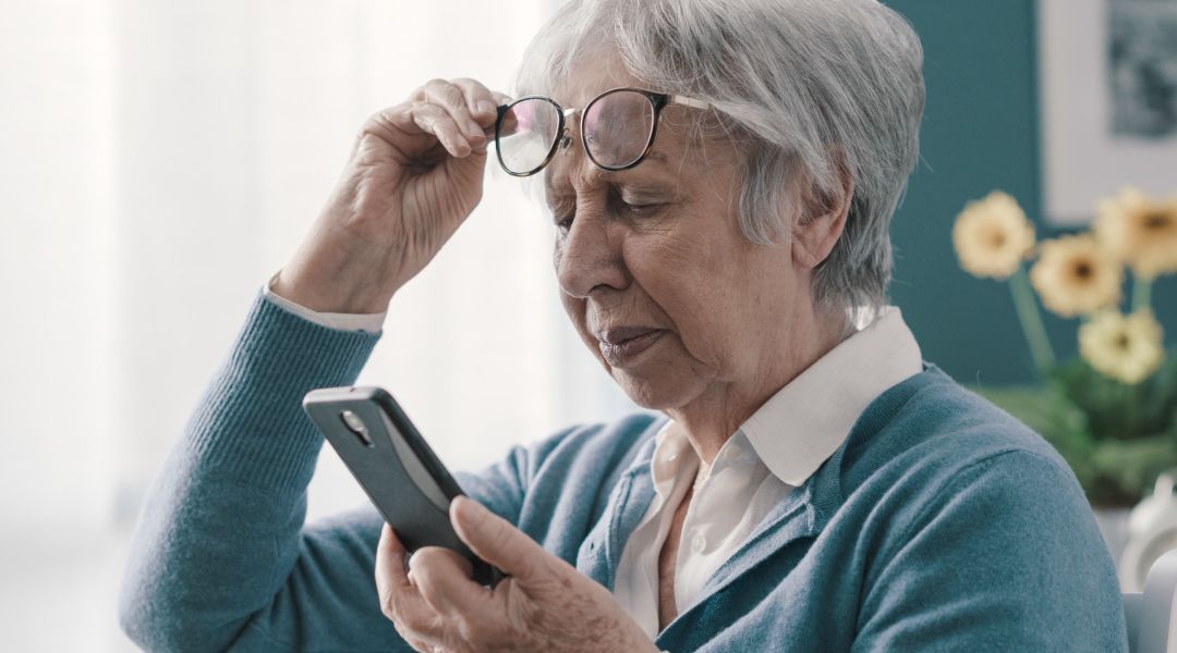 An elderly woman wearing glasses is looking at her cell phone