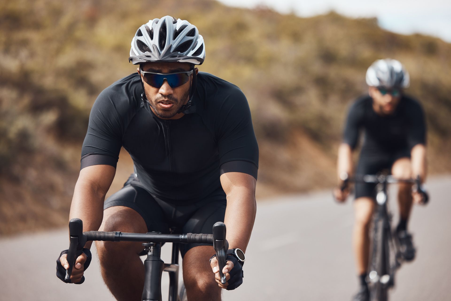 Two people wearing protective eyewear riding bicycles outdoors