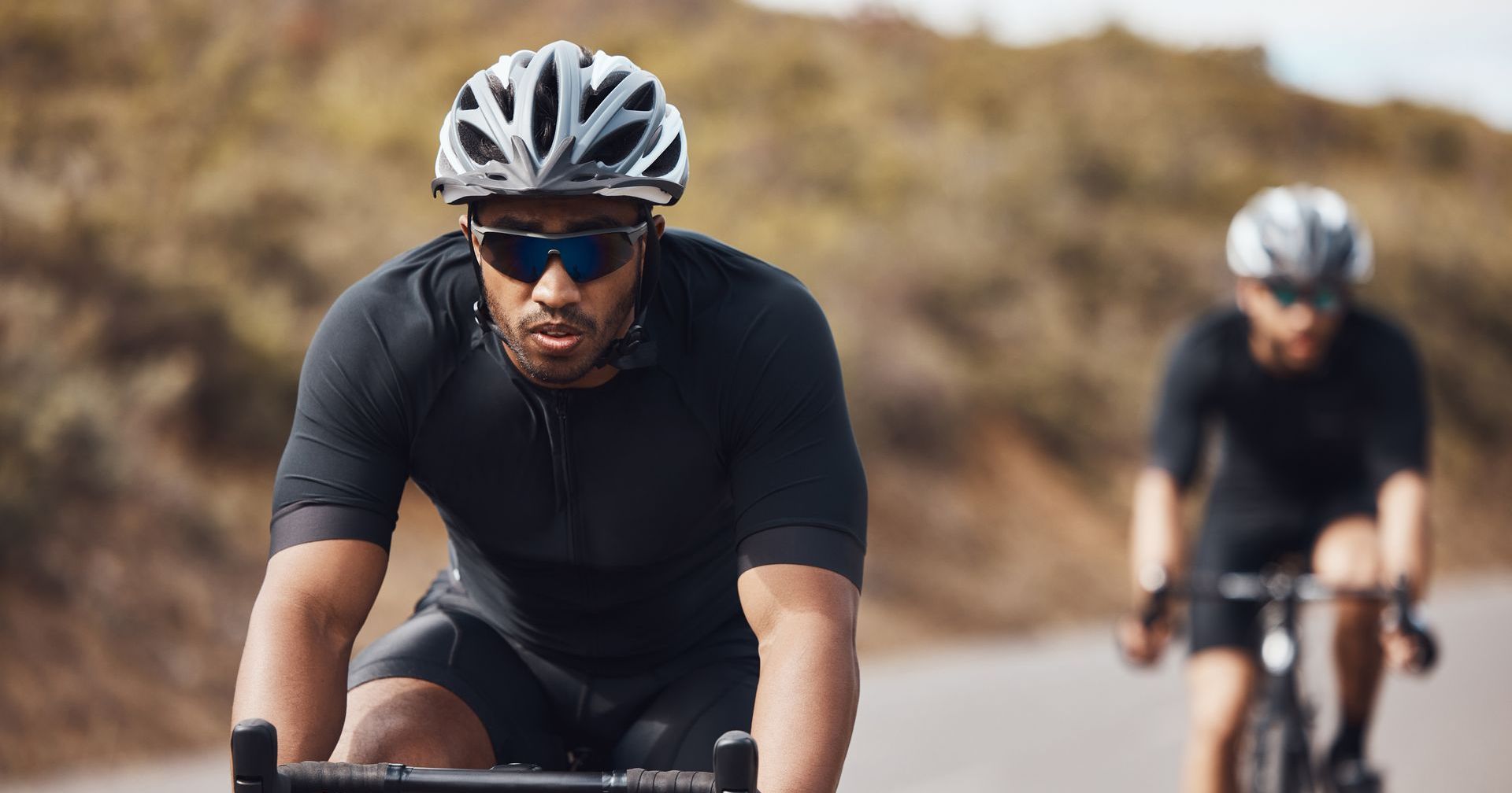 Two people wearing protective eyewear riding bicycles outdoors