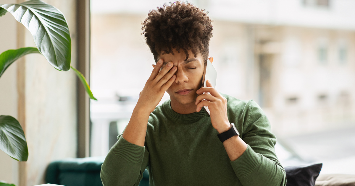 Person on a cellphone dealing rubbing their eyes from an ocular migraine.