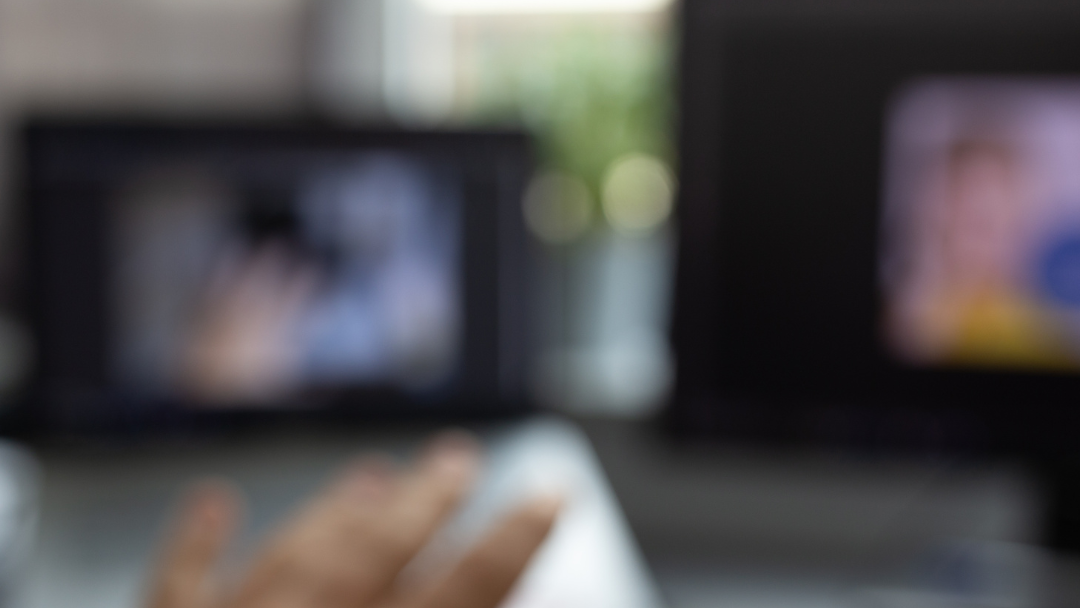 Blurry image of person holding mouse with computers in background
