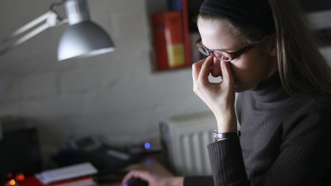 Person rubbing their eyes while looking at a computer screen
