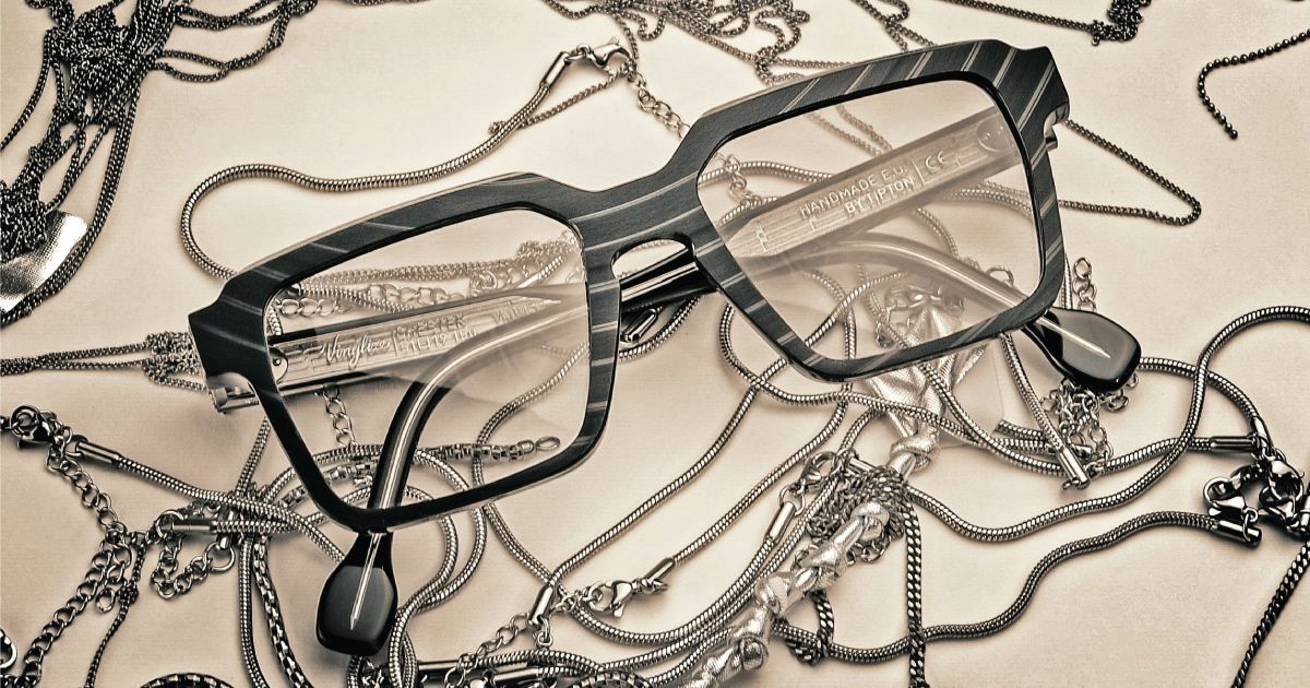 Black eyeglasses resting on tangled silver chains over a beige fabric background