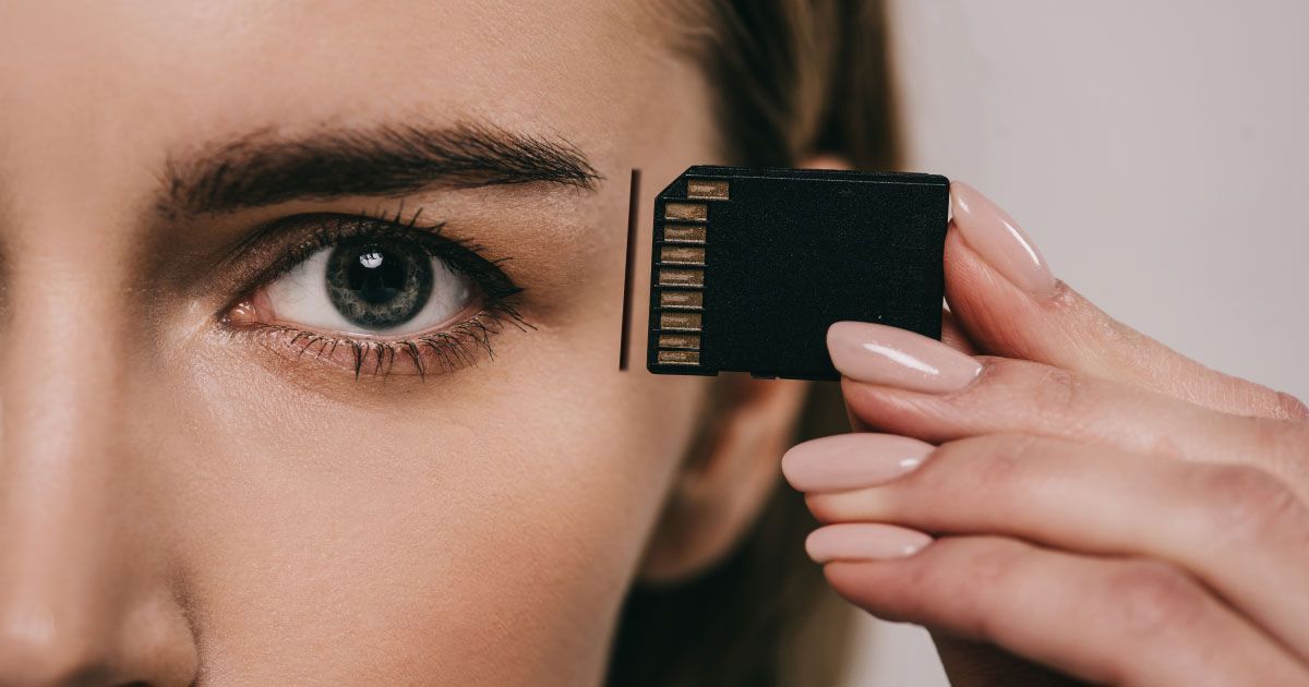 A woman is holding a memory card in front of her eye.