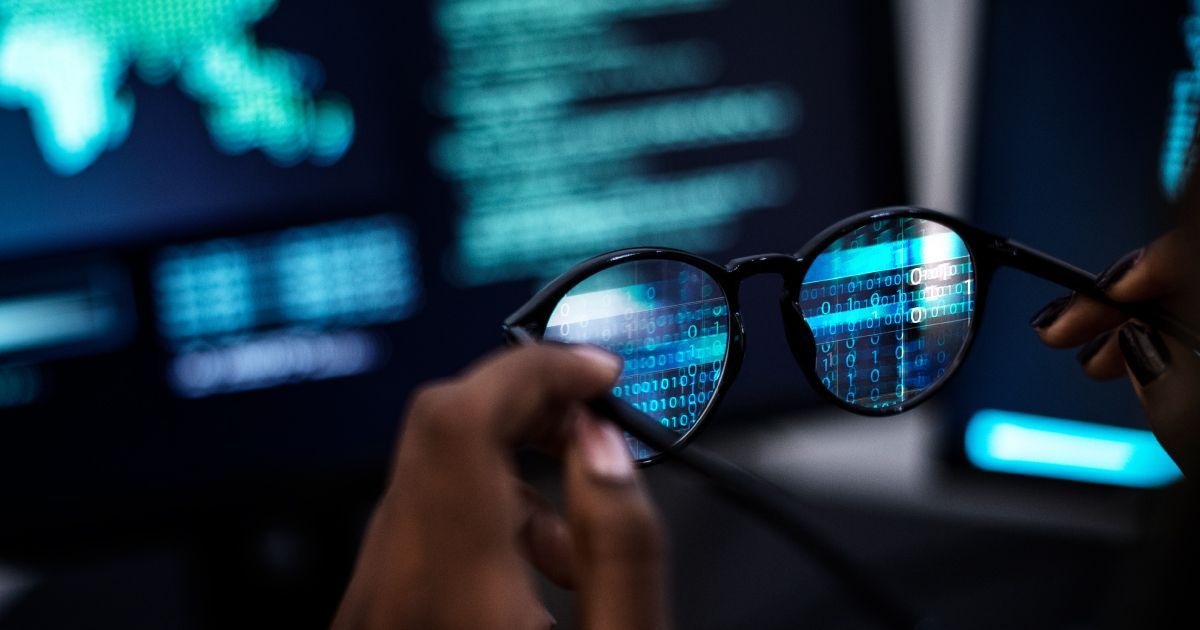 Person holding eyeglasses reflecting lines of code from a computer screen.