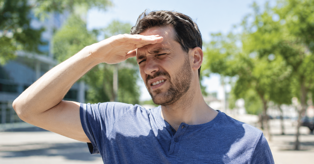 Man shielding his eyes from bright sunlight outdoors in a park