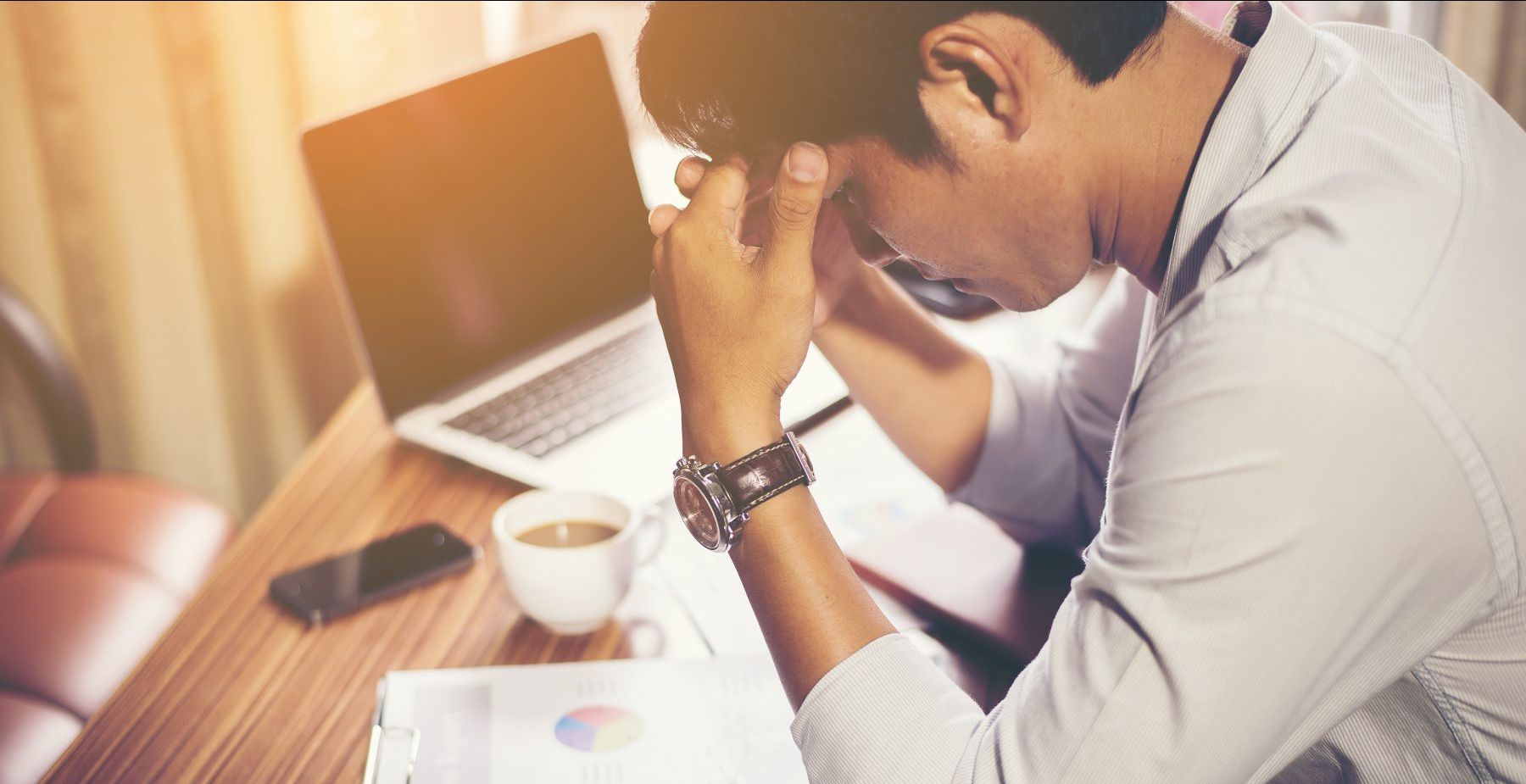 Person sitting at desk with a laptop on it with their hands on their forehead
