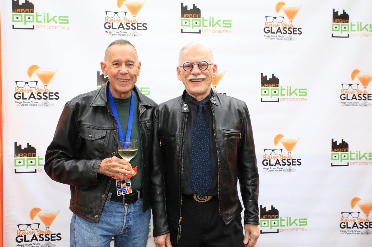 2 people posing in front of logo banner at Raise Your Glasses 2017 Event