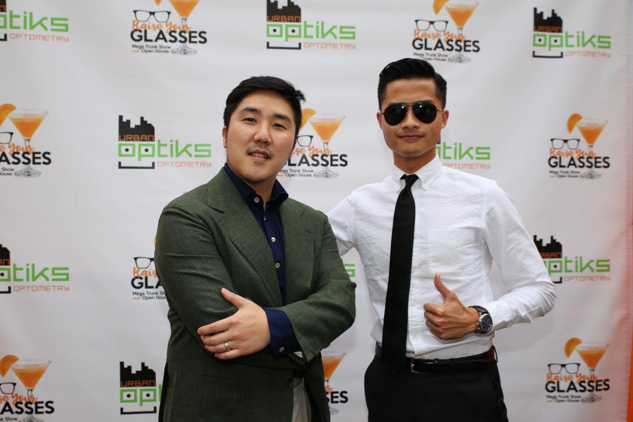 2 people standing outside in front of logo banner at Raise Your Glasses 2017 Event