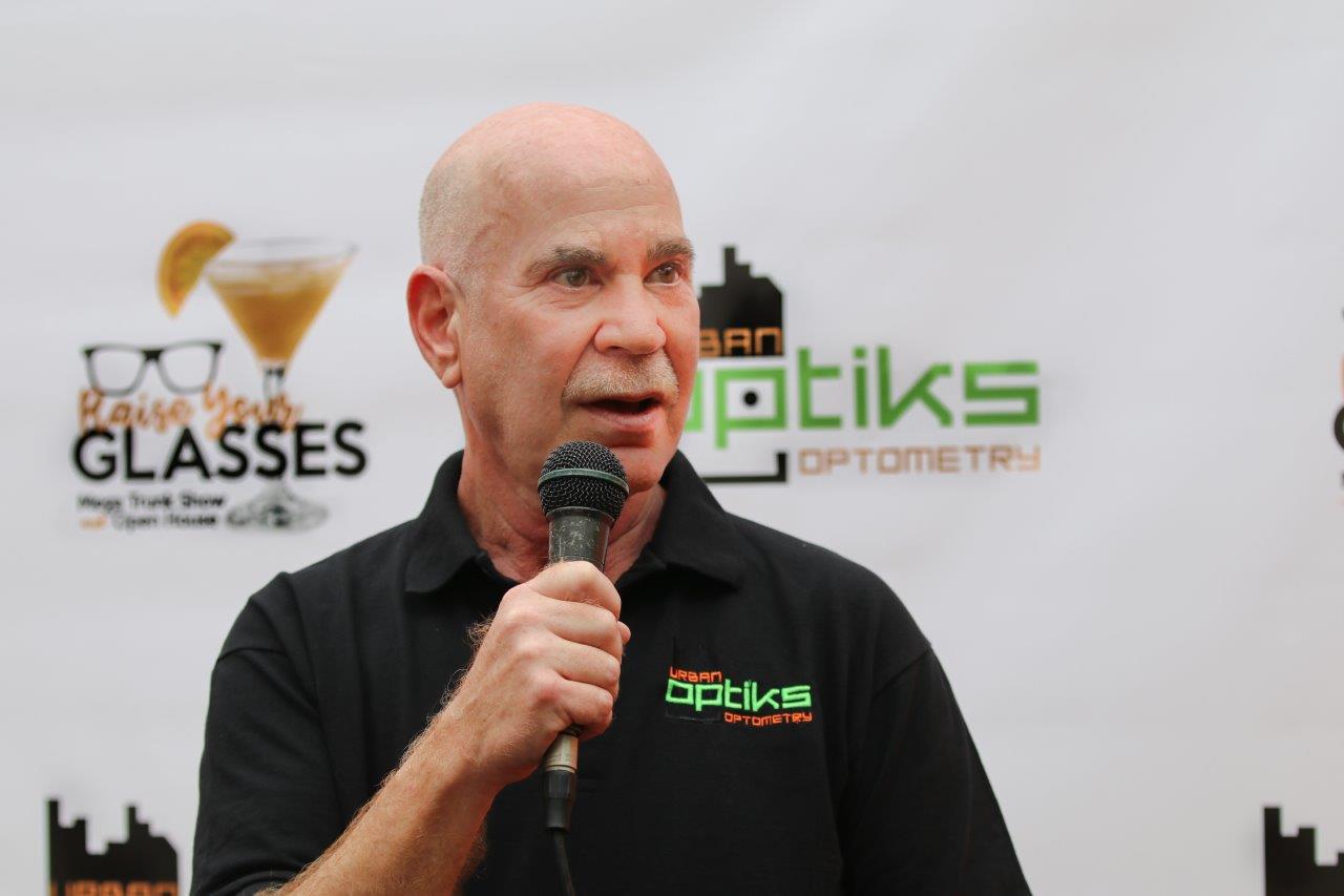 Man in black t-shirt on microphone in front of logo banner