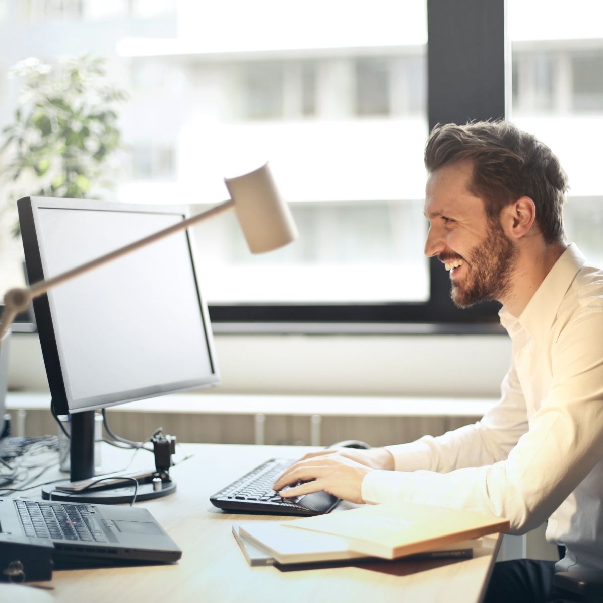 A man sitting at a desk using a computer and smiling