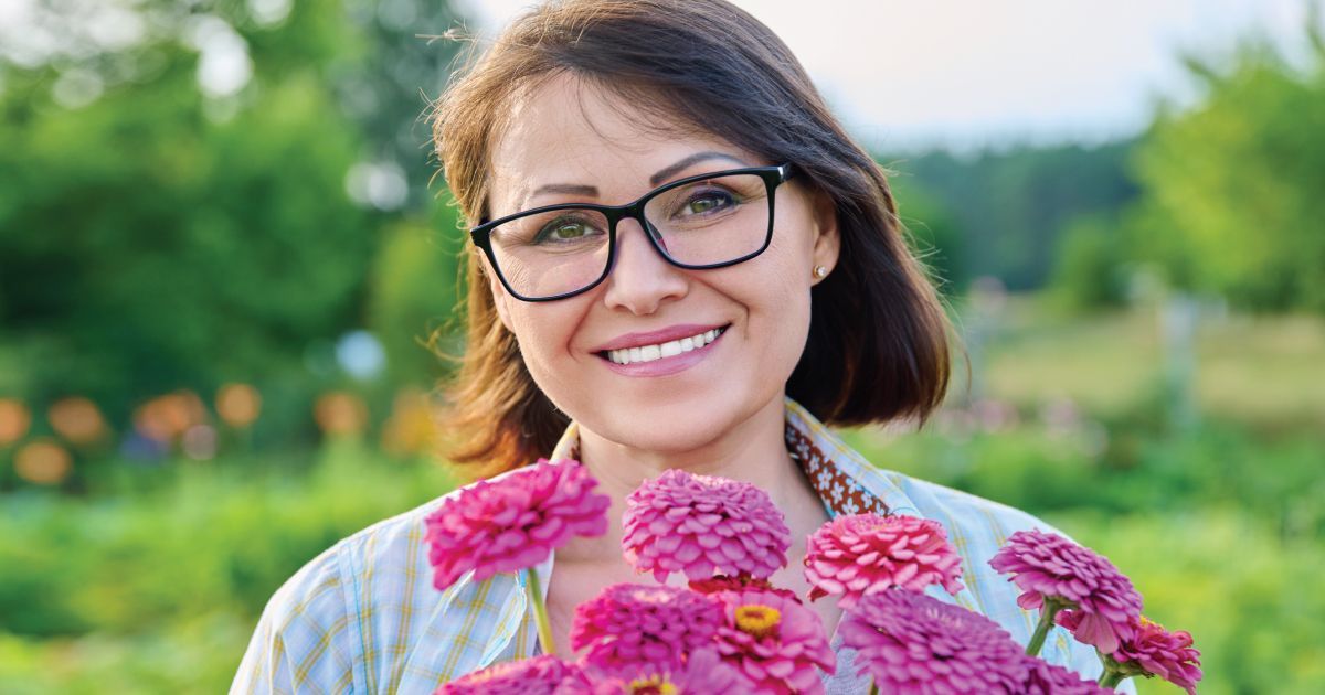 Smiling woman holding pink flowers in a sunny garden