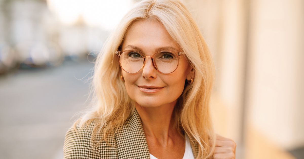 Blonde woman with glasses smiling outdoors.
