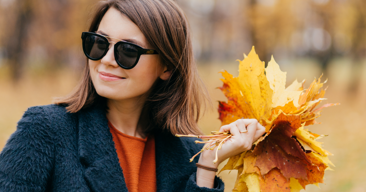 Woman in sunglasses holding a bouquet of autumn leaves outdoors