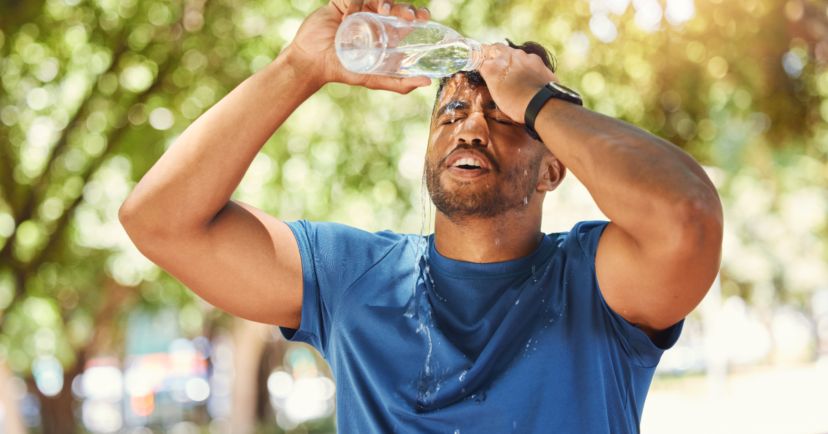 Man in a blue shirt pouring water on his face outdoors in bright sunlight