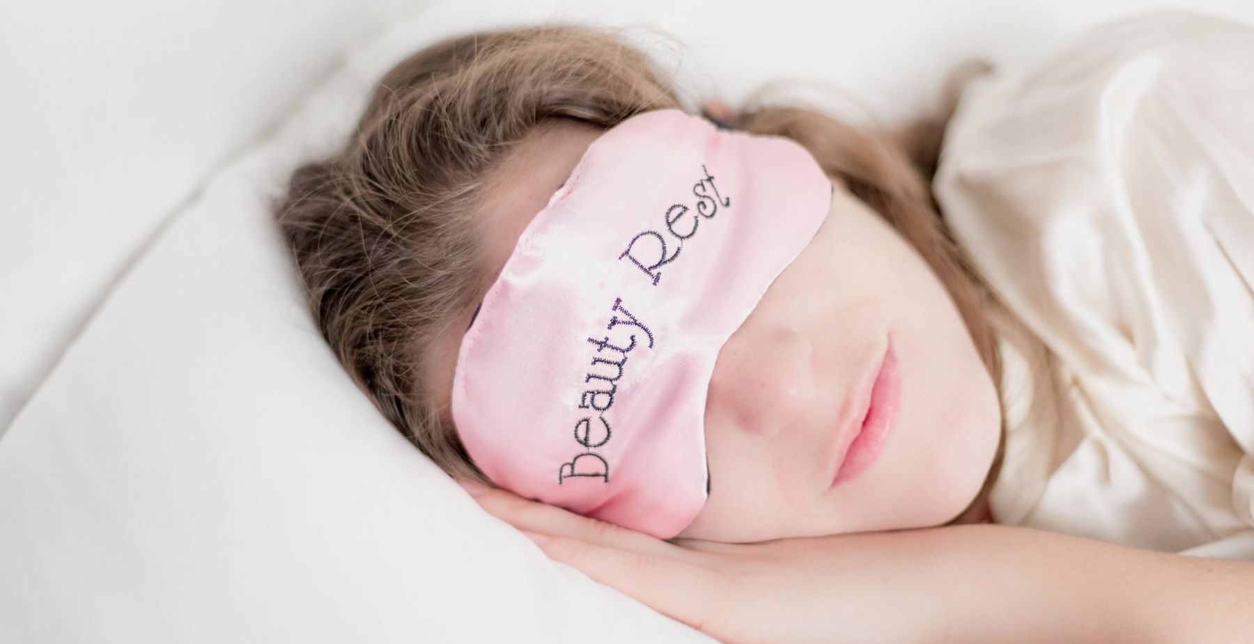 Woman with head on pillow wearing pink eye mask with Beauty Rest written on it