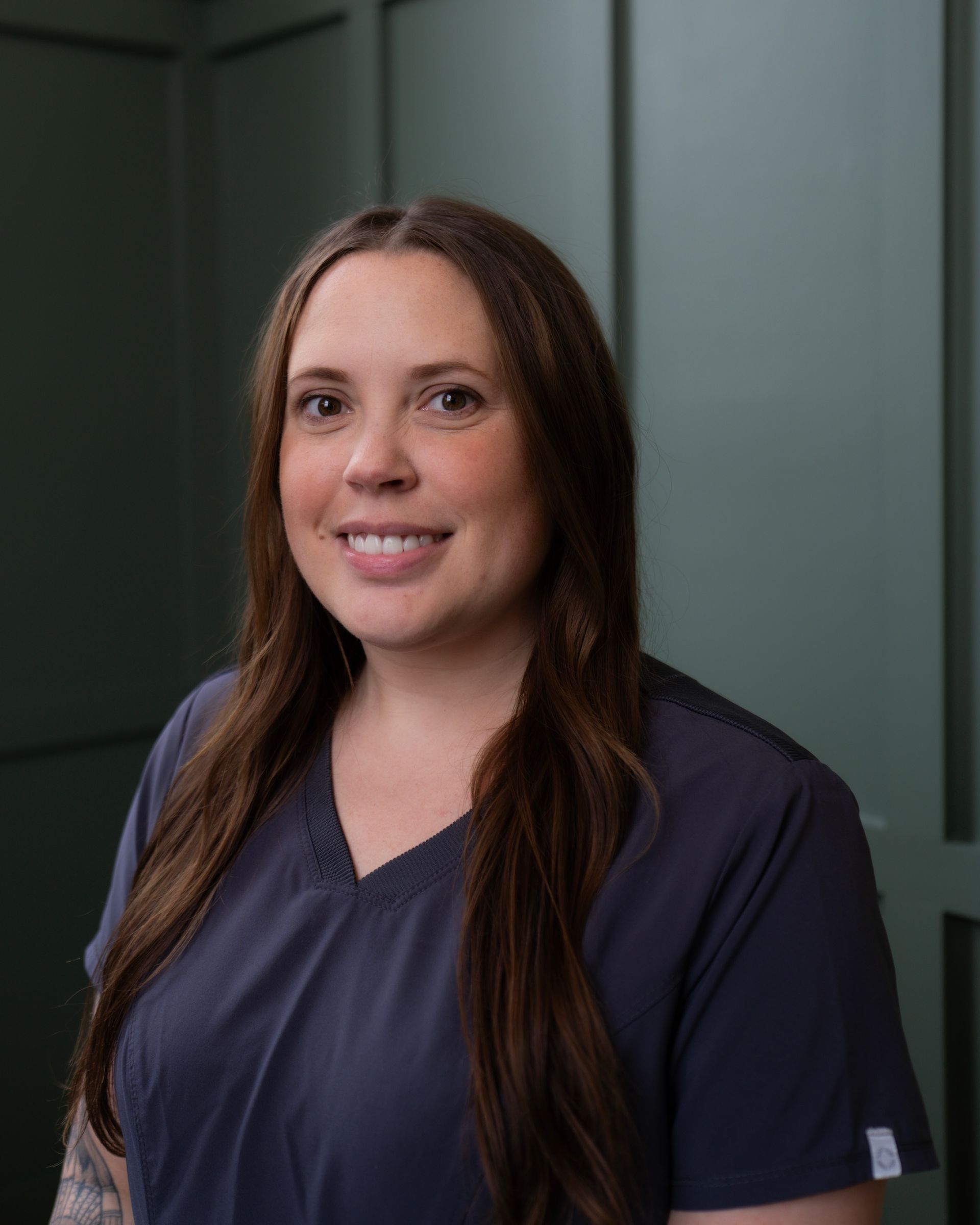 A woman in a blue scrub top is smiling for the camera.