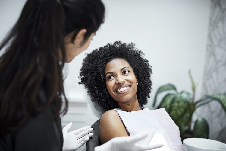 A woman is sitting in a dental chair talking to a dentist.