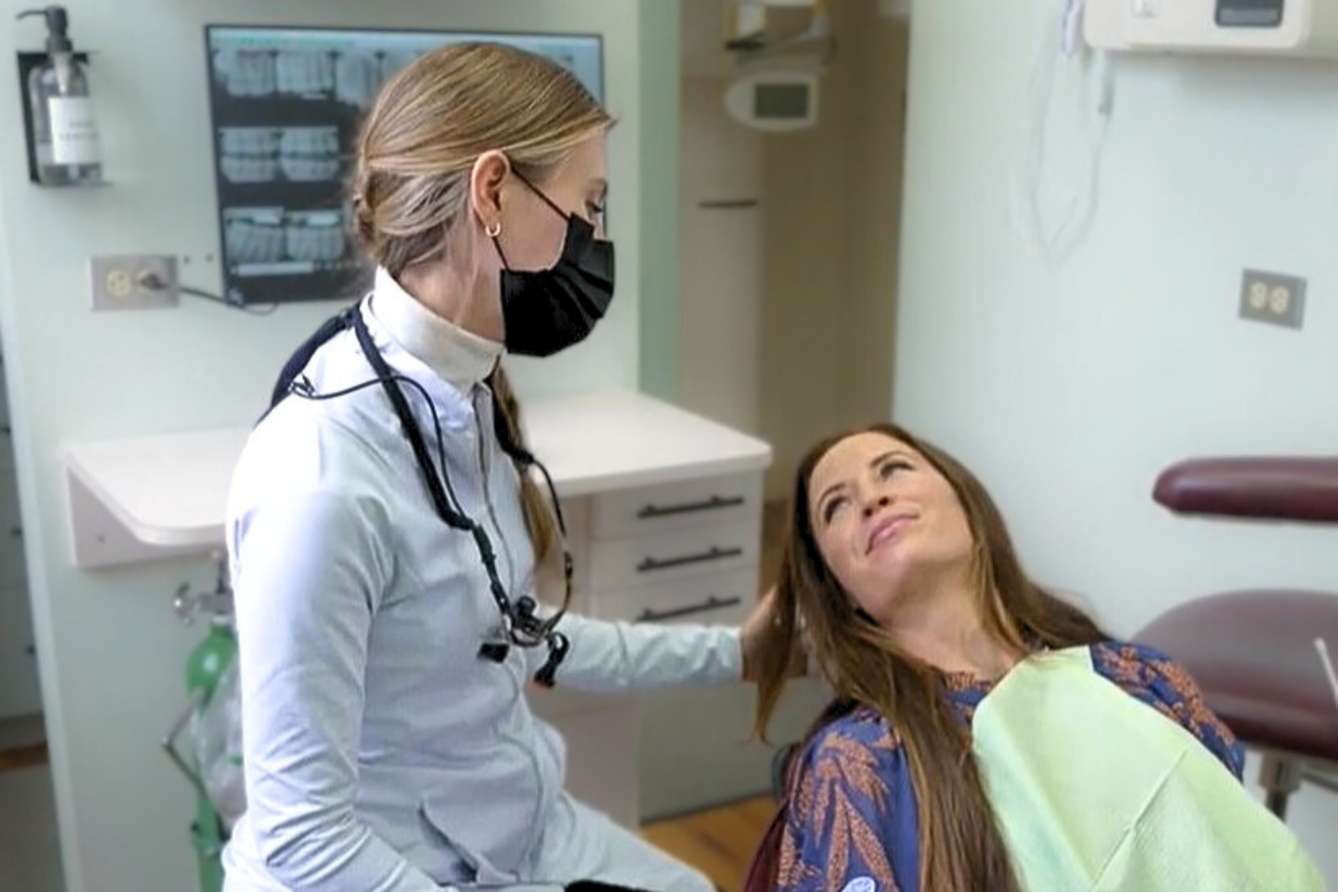 A dentist is talking to a patient in a dental chair while holding a model of a skull.