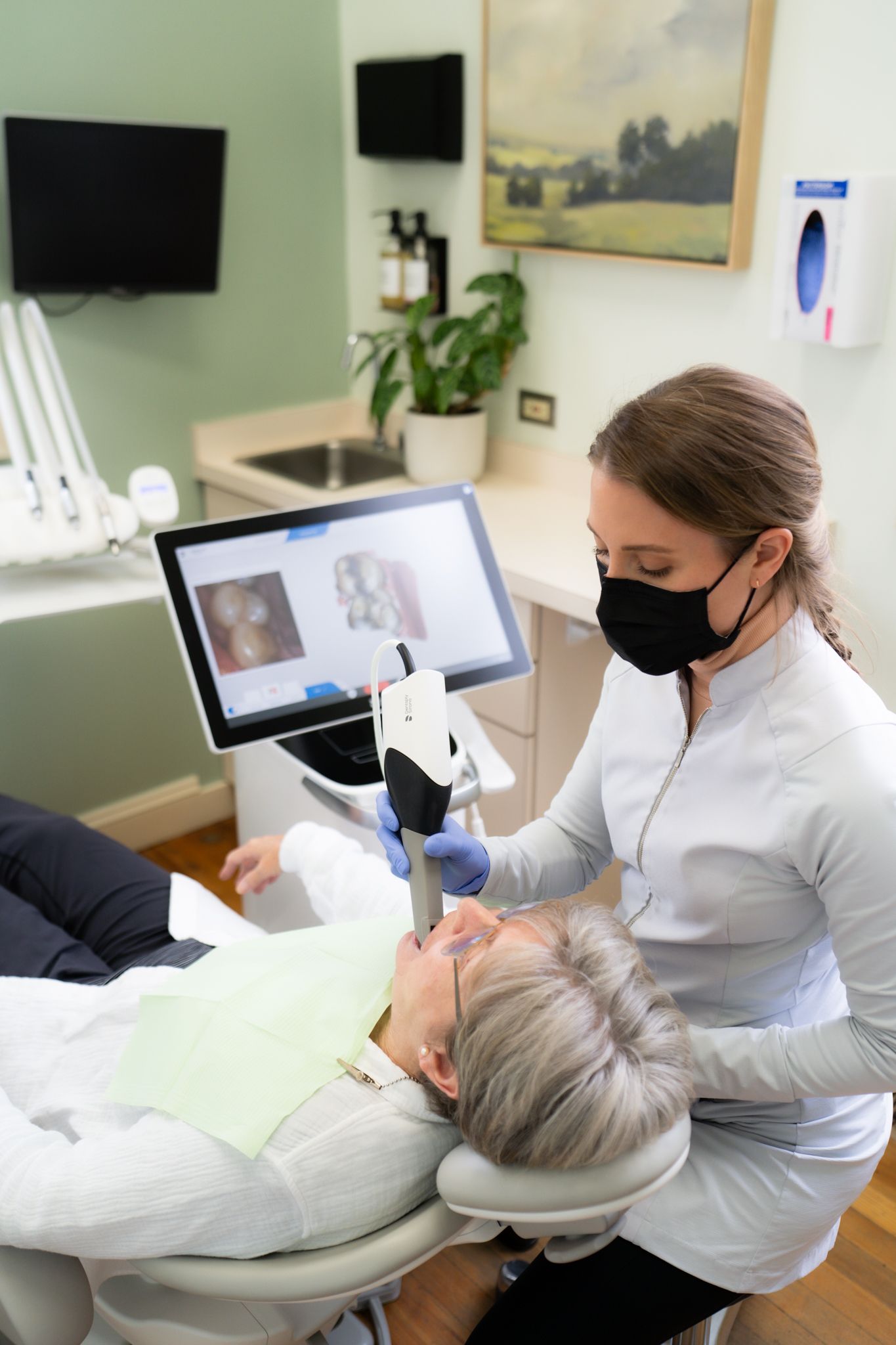 An elderly woman is sitting in a dental chair looking at her teeth in a mirror.