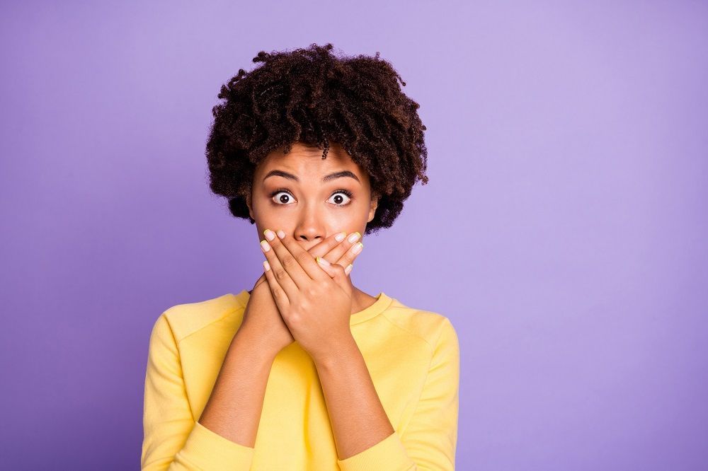 A woman in a yellow sweater is covering her mouth with her hands.