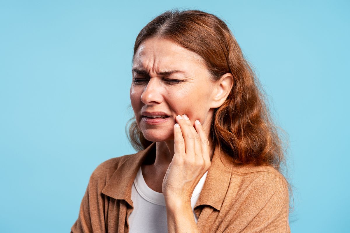 Woman grimacing and holding her cheek against a blue background