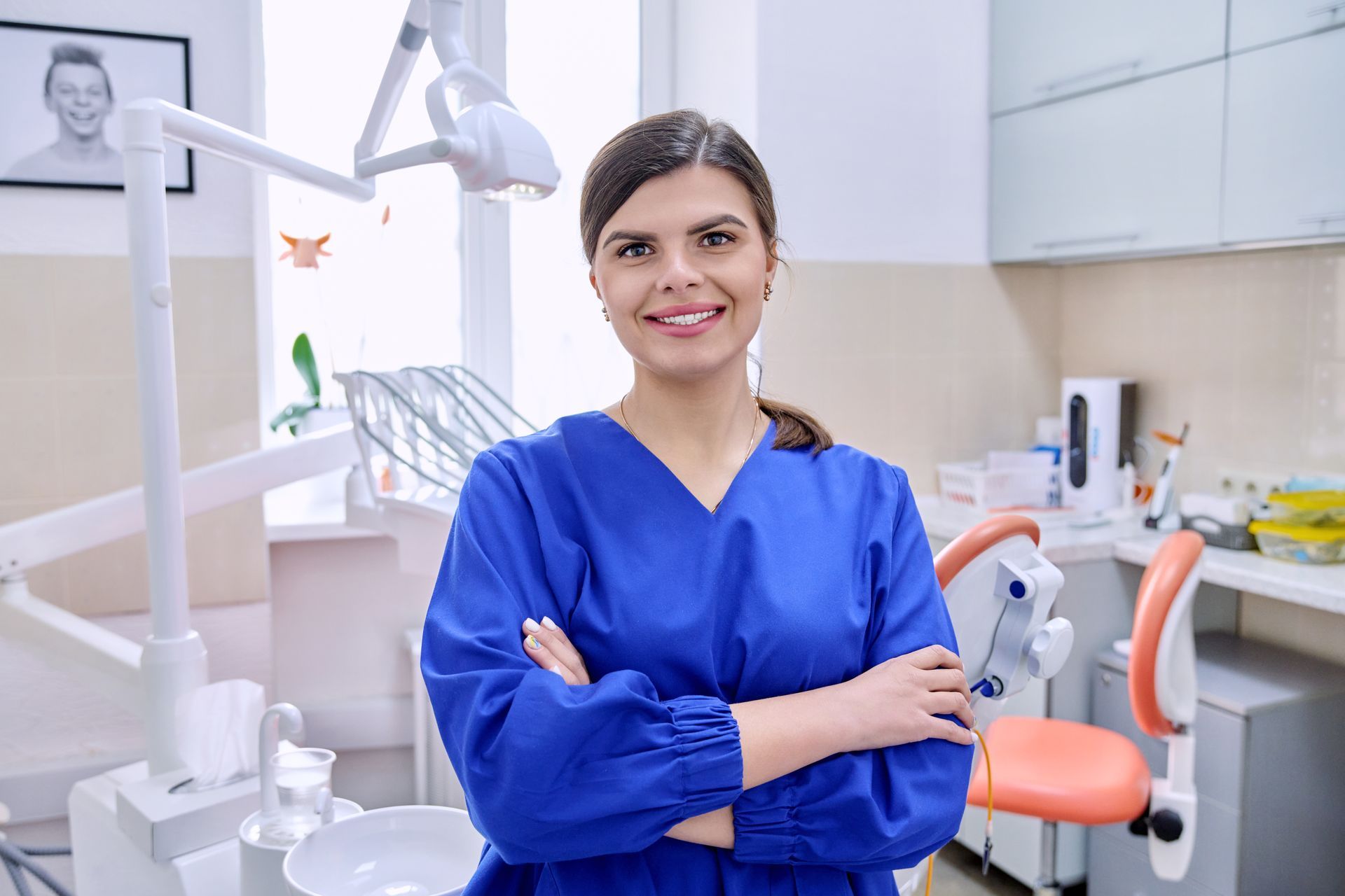 A female dentist is standing in a dental office with her arms crossed.