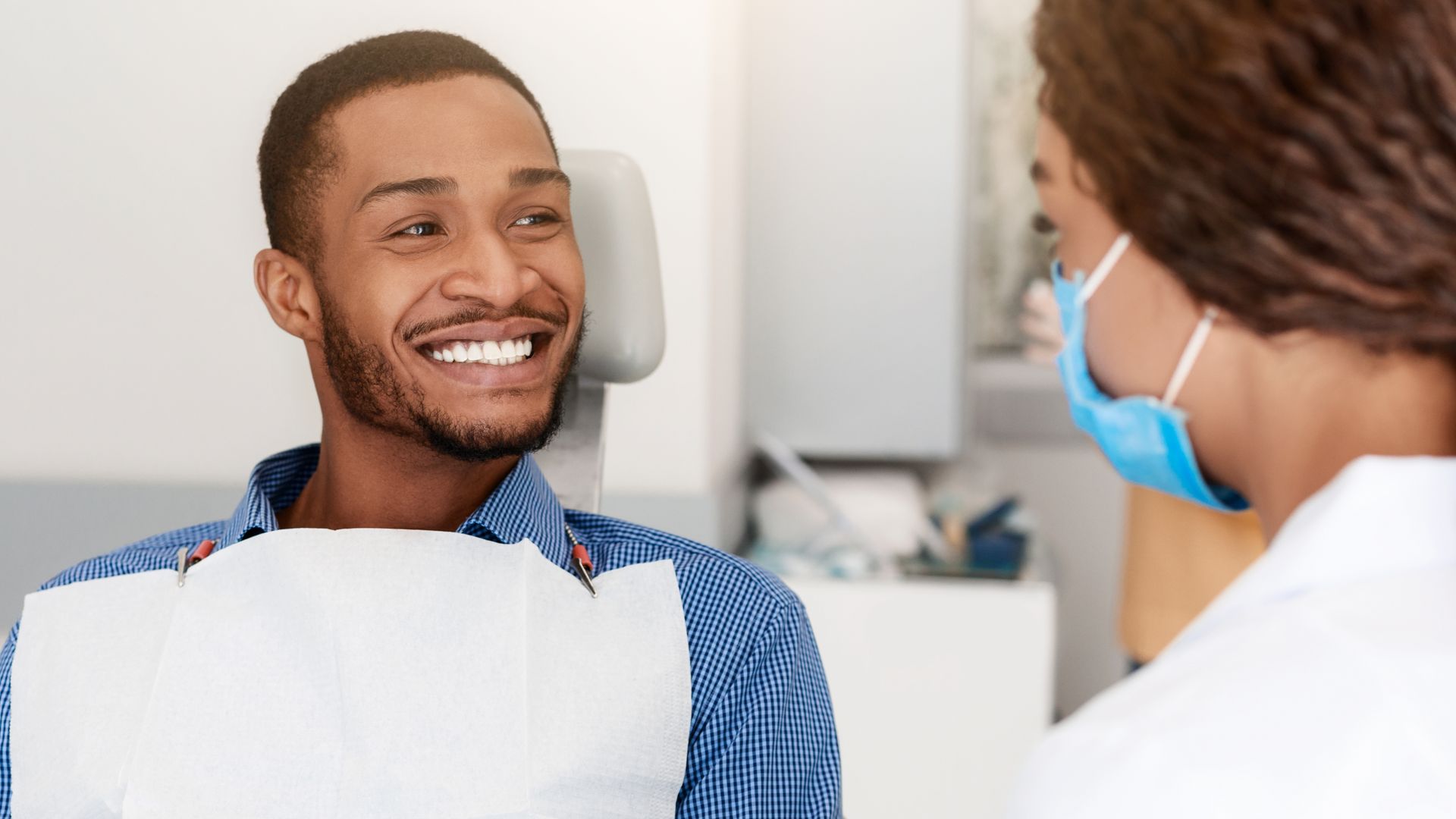 A man is smiling while sitting in a dental chair talking to a dentist.