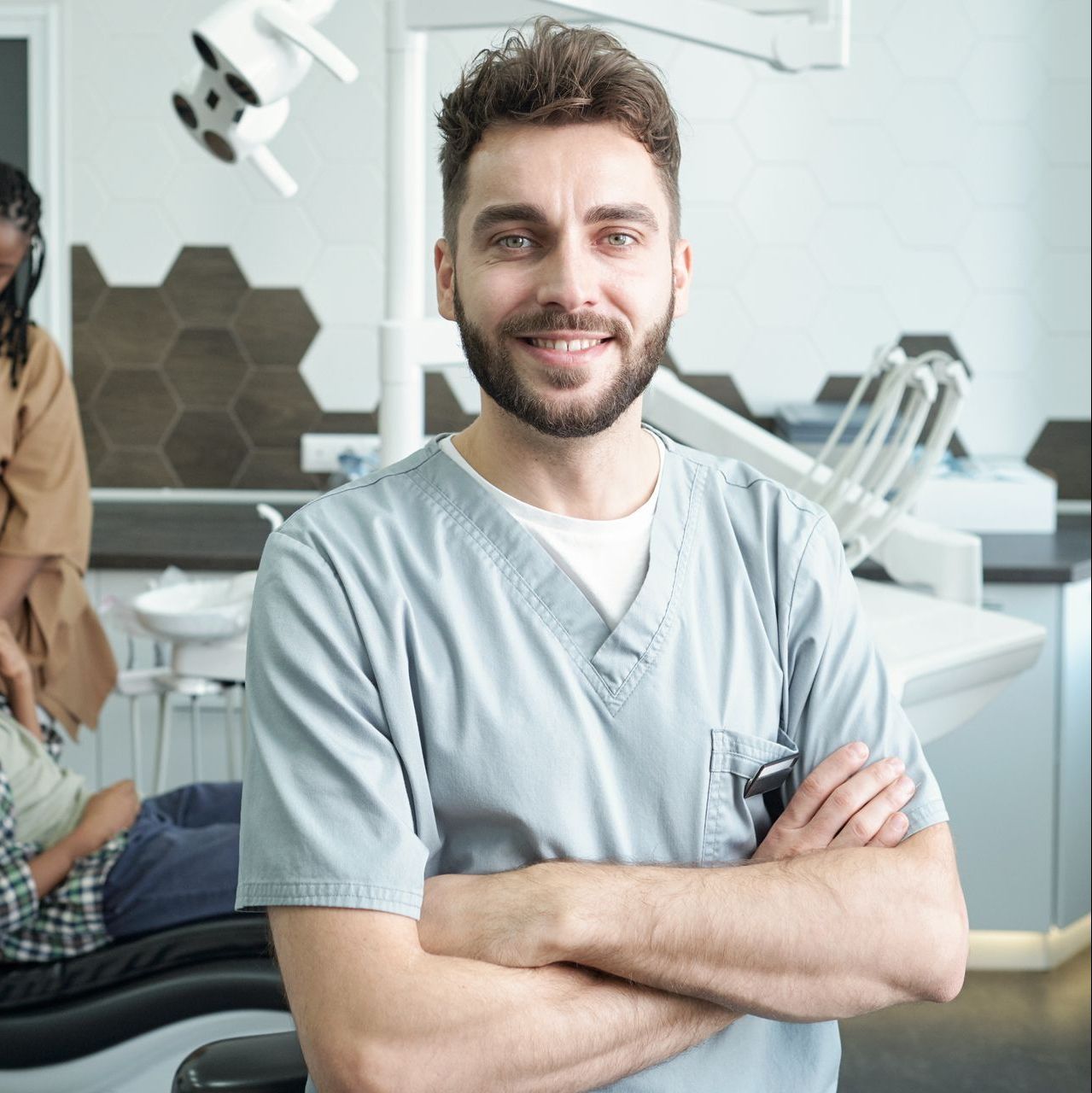 A man with a beard is standing in a dental office with his arms crossed.
