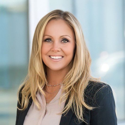 Smiling blonde woman in a black blazer against a soft blue background