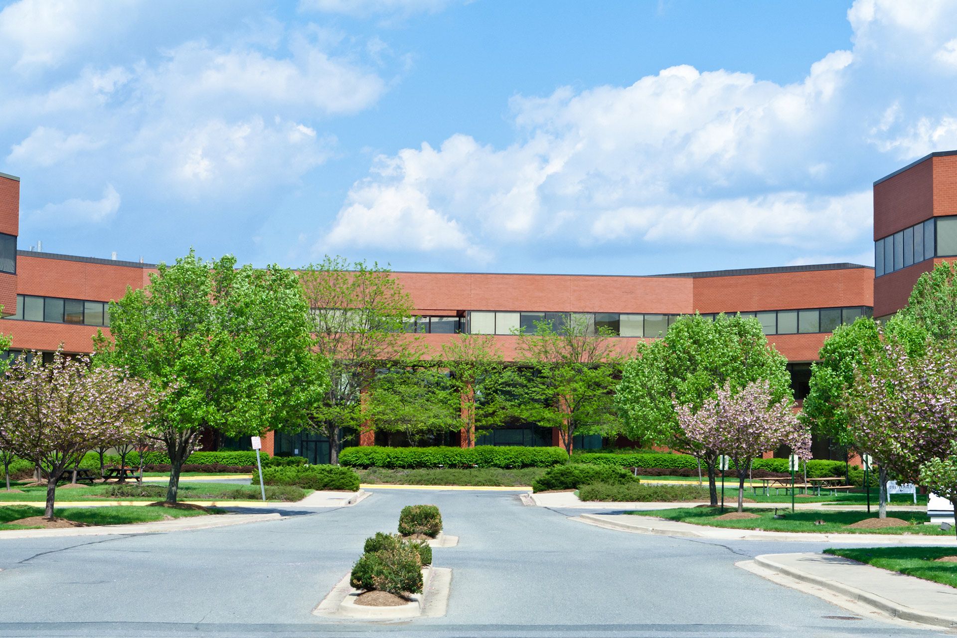 Brick office building with trees and a blue sky with clouds.