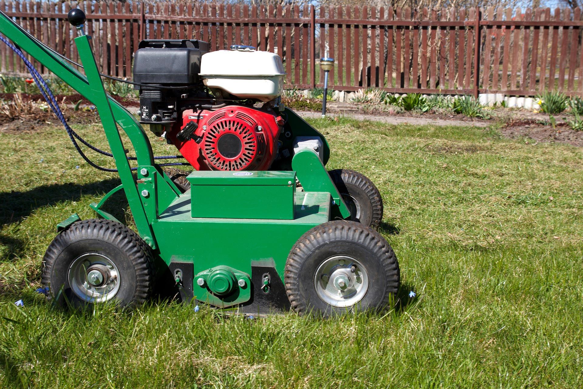 Green lawn aerator with a red engine on grass.