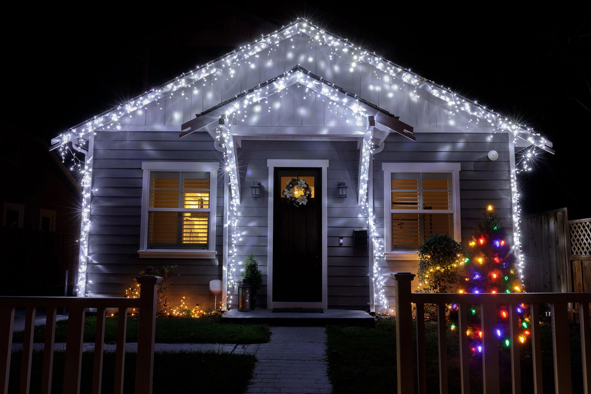 House decorated with white Christmas lights; colorful tree lights.