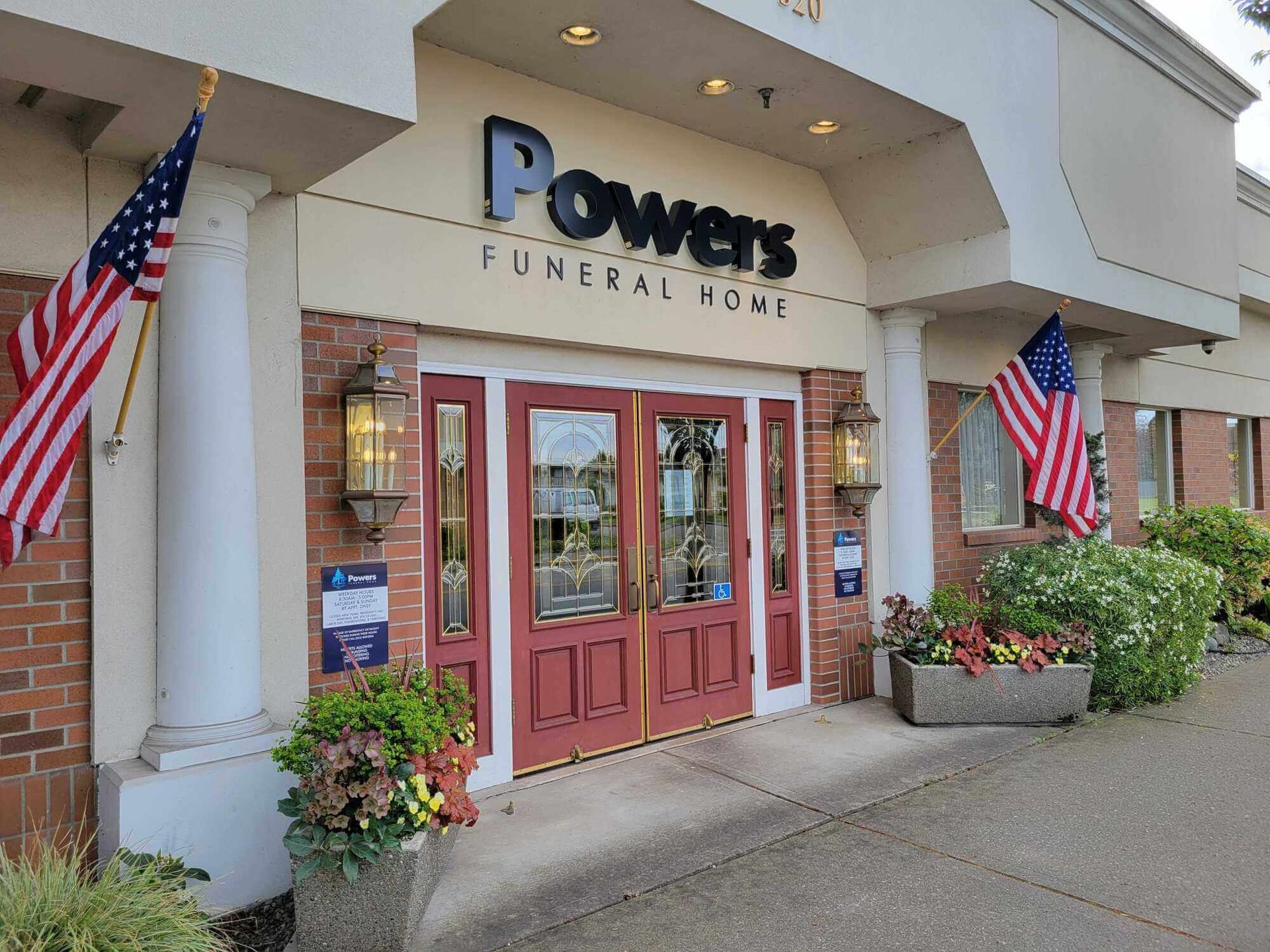 Powers Funeral Home entrance with American flags, red doors, and potted flowers