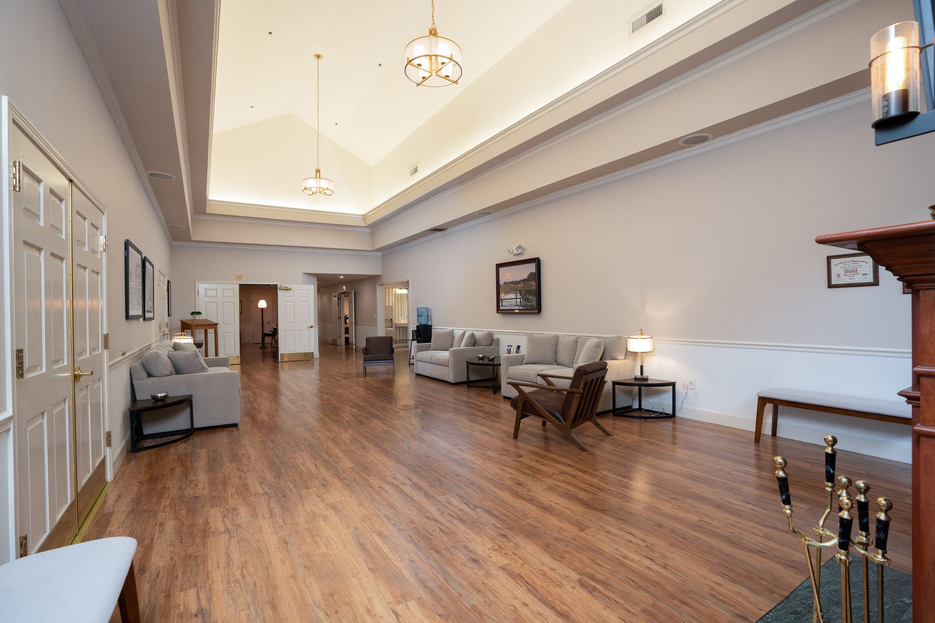 Spacious modern lobby with wood floors, white walls, seating area, and chandeliers.